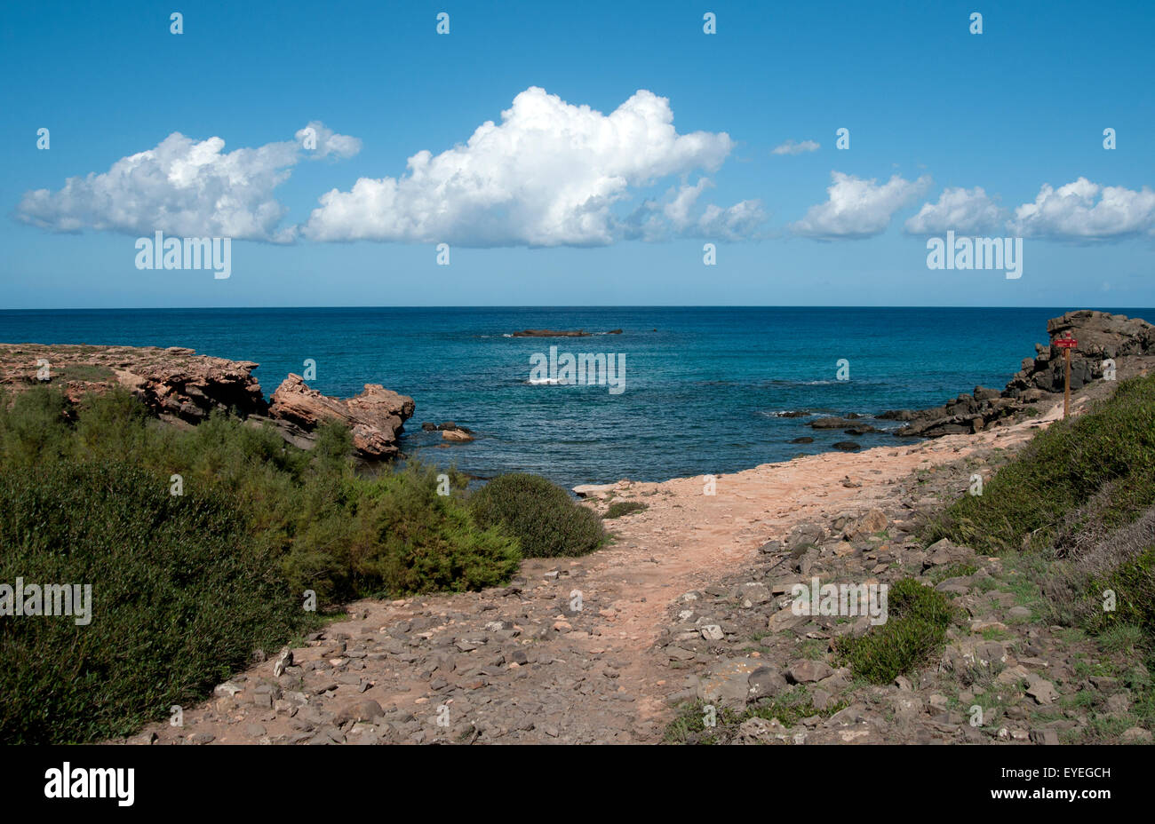 Vista sul mare e soffici nuvole bianche dalla riva di una appartata spiaggia ghiaiosa sull isola di Minorca spagna Foto Stock