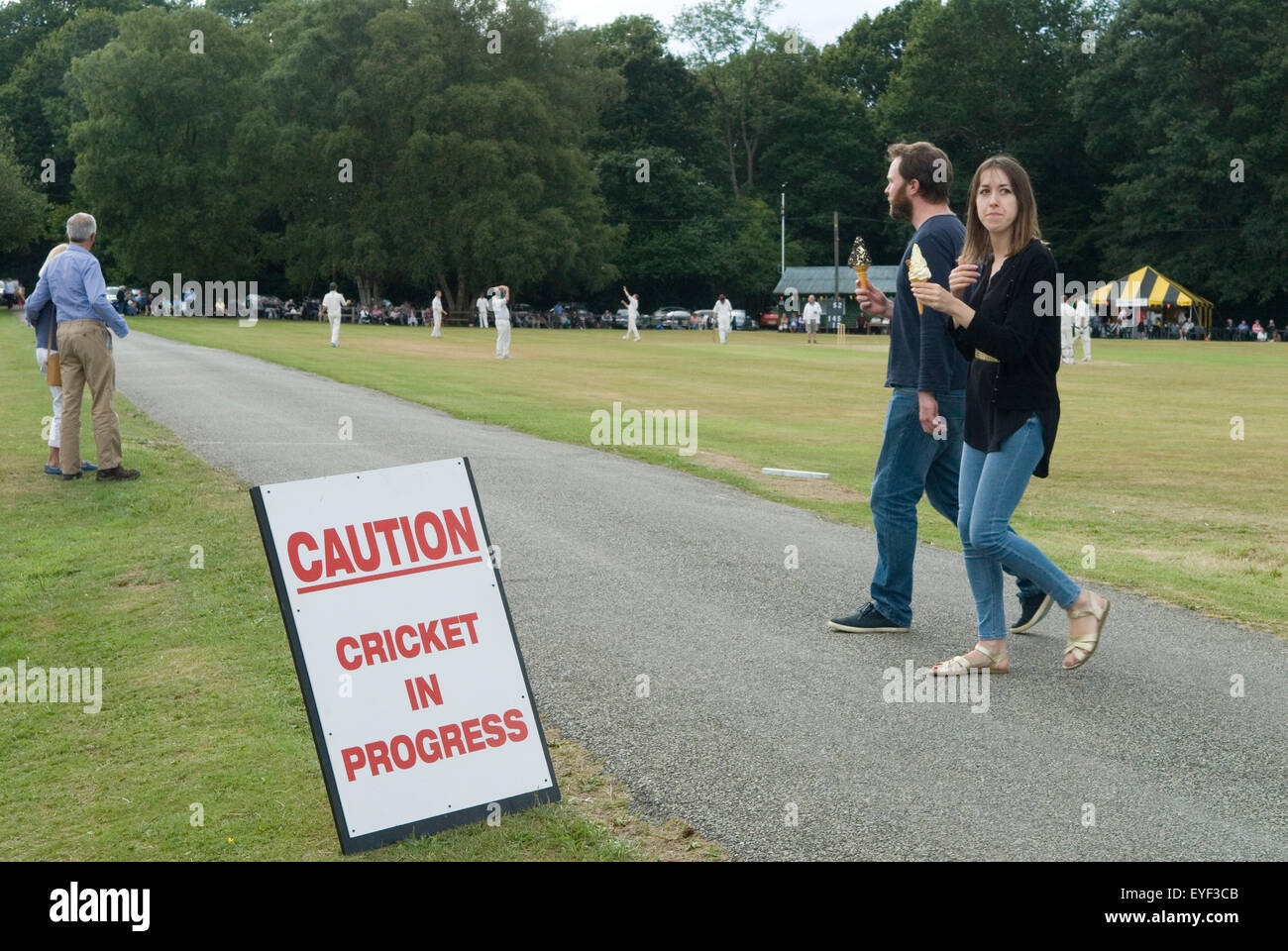 Villaggio di Ebernoe, riserva naturale e comune. Una strada passa attraverso il comune, i conducenti di auto sono avvertiti attenzione Cricket in corso. Una coppia che mangia un gelato si gode l'annuale partita di cricket di St Jame's Day (25 luglio). Ebernoe CC contro Wessex Pilgrims CC. Ebernoe, West Sussex 2017 Inghilterra 2010s UK HOMER SYKES Foto Stock