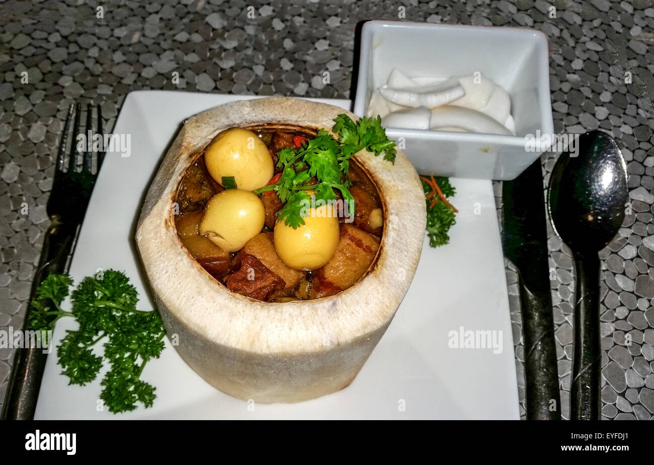 Saporito spezzatino di maiale servito con salsa di cocco, uova di quaglia e fette di cocco fresco, in un fresco buccia di cocco. Foto Stock