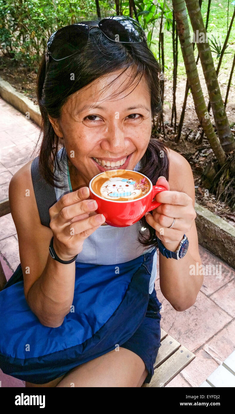 Latte macchiato di fantasia con un Hello Kitty design di essere apprezzato da un locale Singapore donna alla guarnitura piena di fagioli, una caffetteria/deli Foto Stock