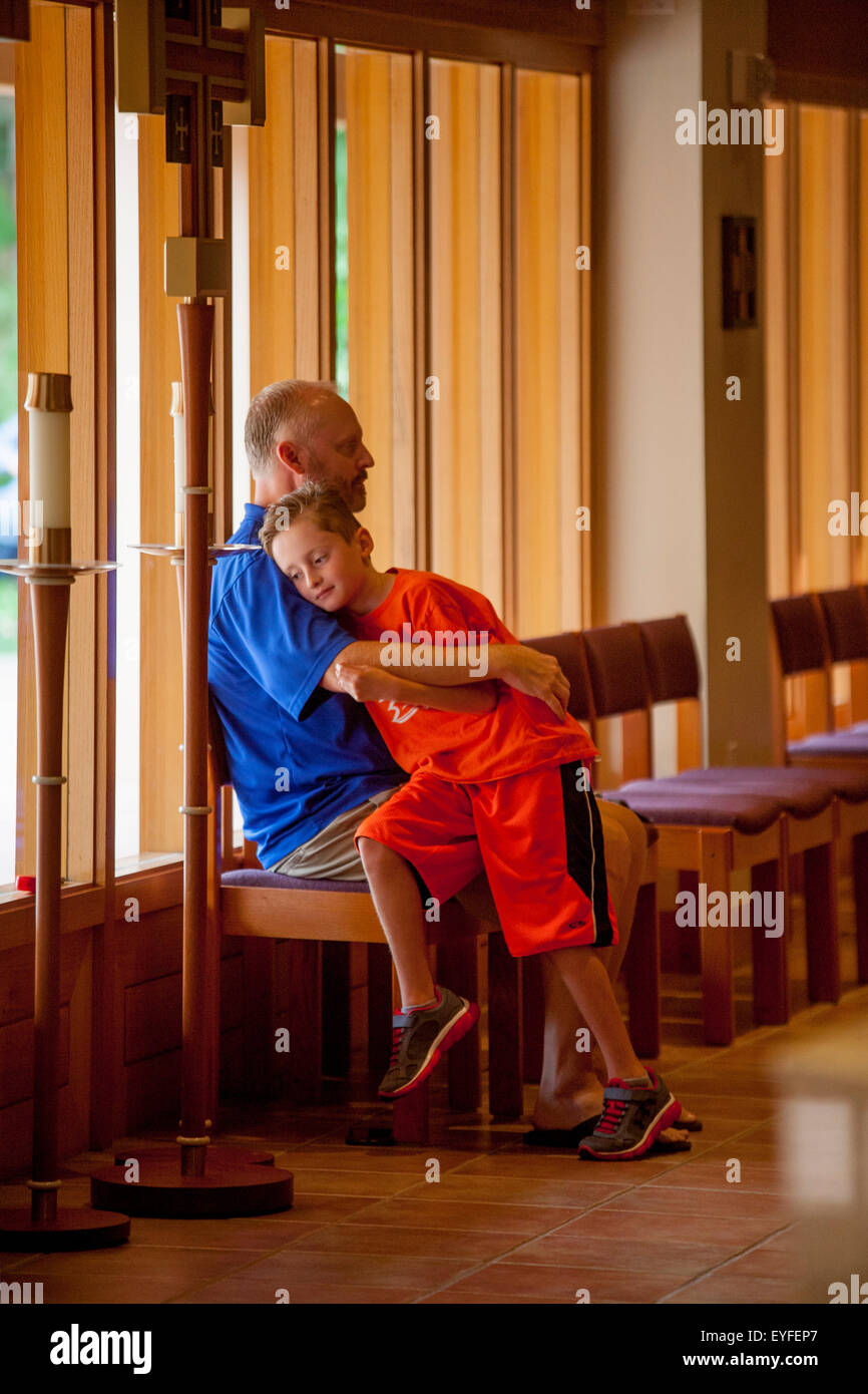 In attesa di massa per iniziare, un padre abbraccia il suo figlio nella fila posteriore di una Laguna Niguel, CA, chiesa cattolica. Nota croce a sinistra. Foto Stock