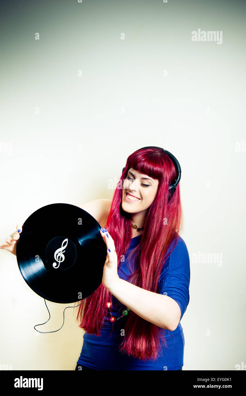 Giovane donna graziosa ballando con le cuffie e dischi in vinile con chiave di violino simbolo telaio verticale Foto Stock