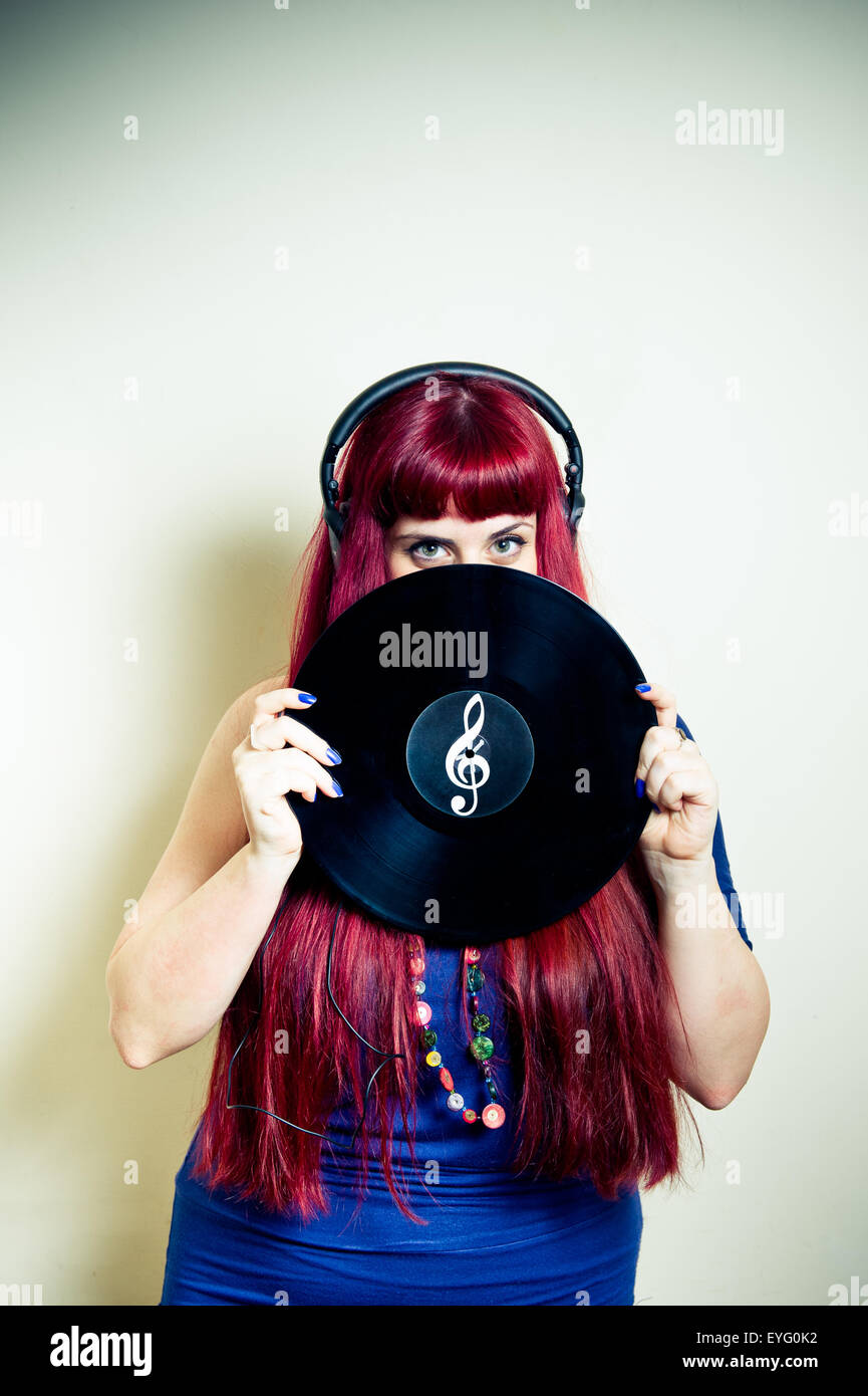 Giovane donna graziosa guardando con cuffie e dischi in vinile con chiave di violino simbolo telaio verticale Foto Stock
