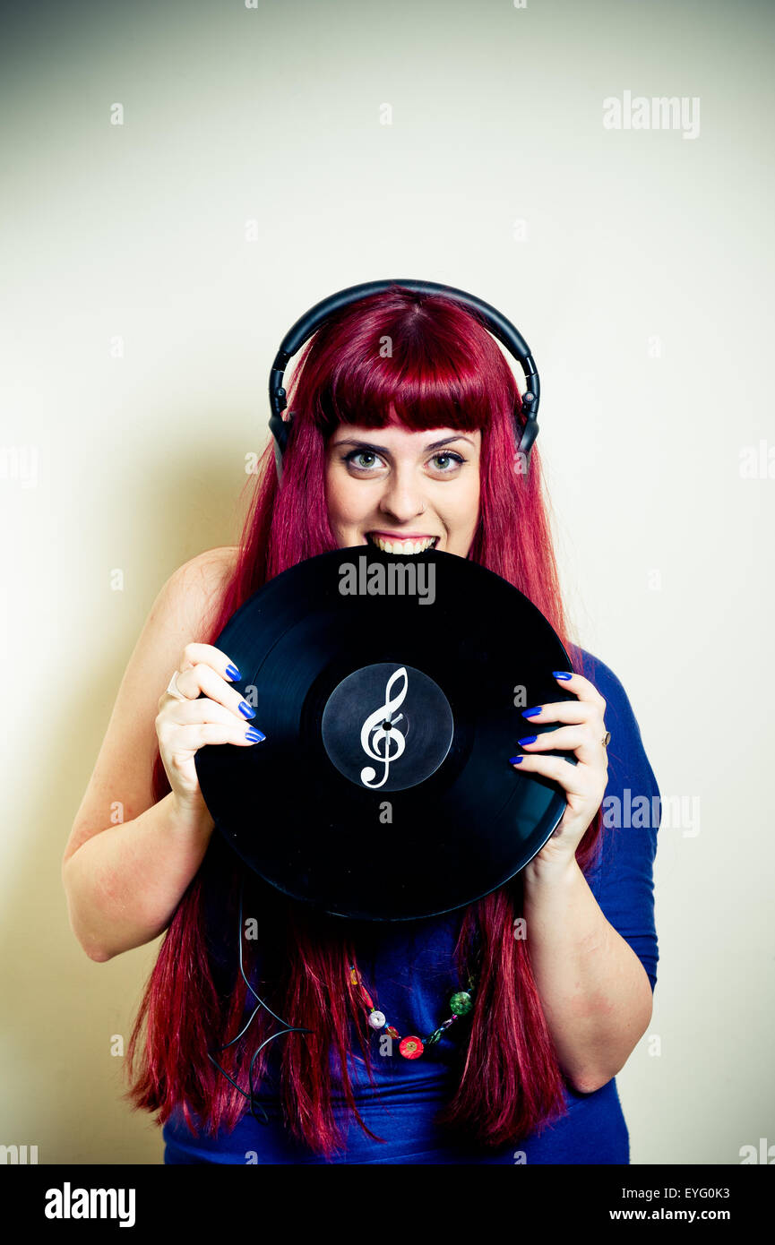 Giovani pretty redhead Donna con cuffie di mordere dischi in vinile con chiave di violino simbolo Foto Stock