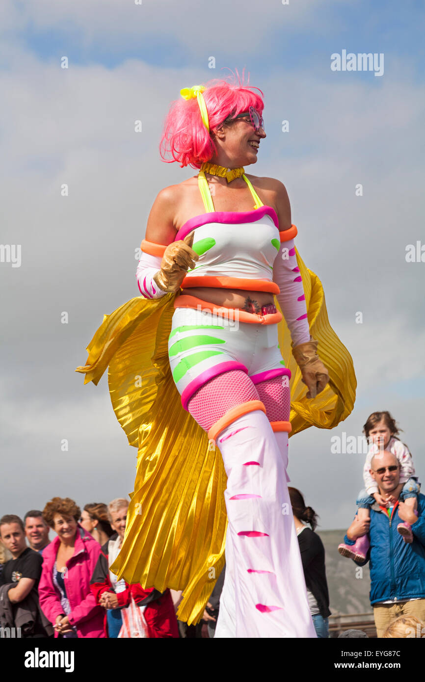 Swanage sfilata di carnevale in luglio con il tema di supereroi - stilt walker. Donna persona in piedi su palafitte. Foto Stock