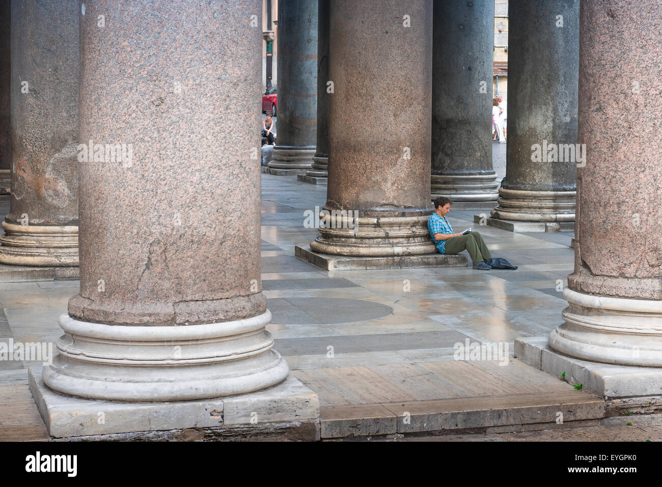 Uomo solo che legge la città, vista di un uomo seduto da solo sotto l'antico portico del Pantheon nel centro di Roma e la lettura di un libro, Italia. Foto Stock