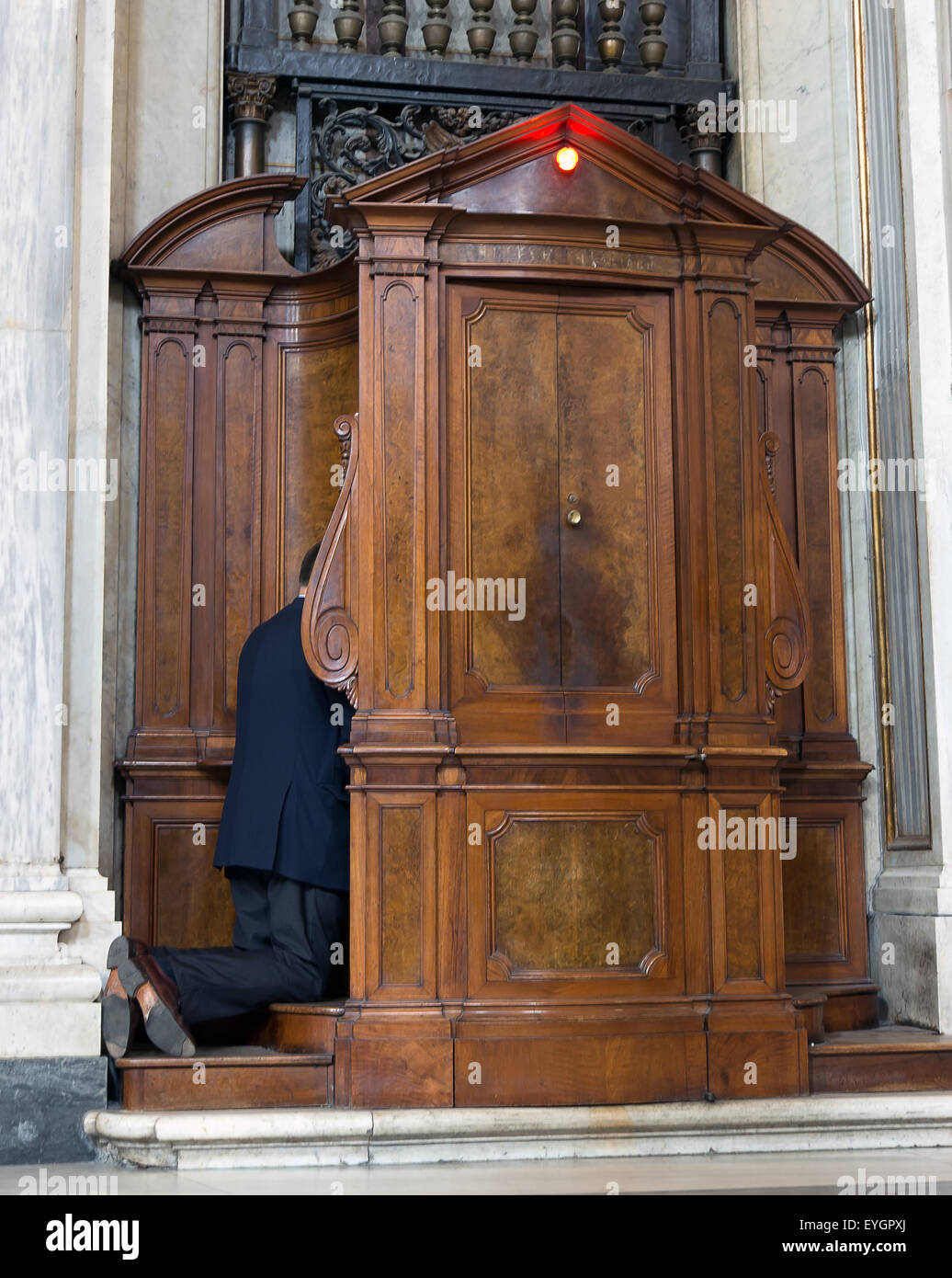 Uomo in ginocchio in confessionale in chiesa Foto Stock