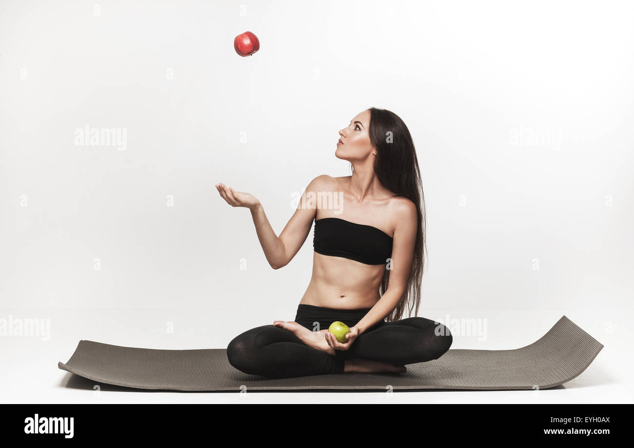 Bruna giovane donna seduta sul materassino yoga. Donna che mantiene apple. Uno stile di vita sano foto del Caucaso modello fitness isolati su wh Foto Stock