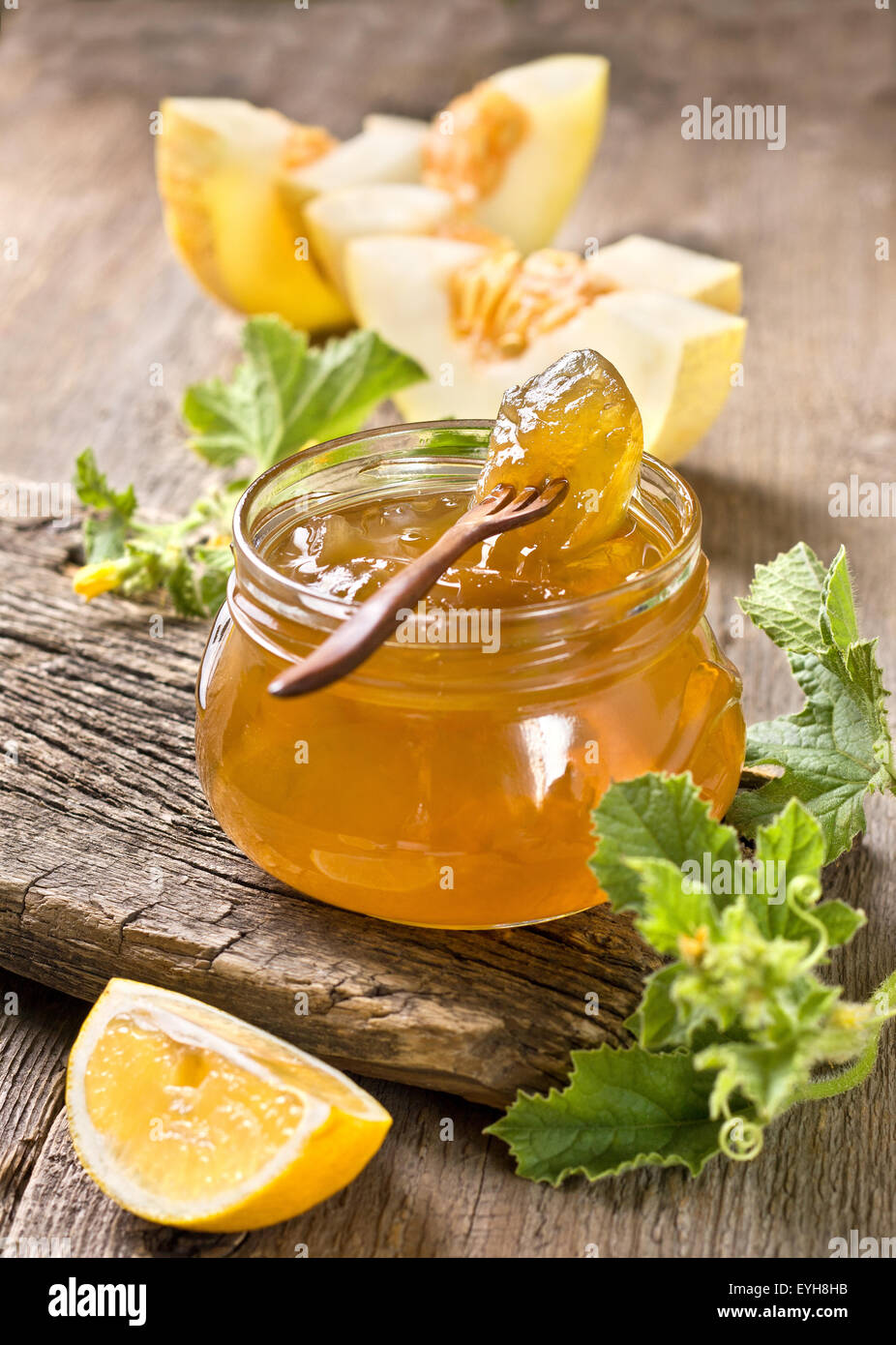 Melone marmellata in un barattolo di vetro, fette di limone, melone su uno sfondo di legno Foto Stock