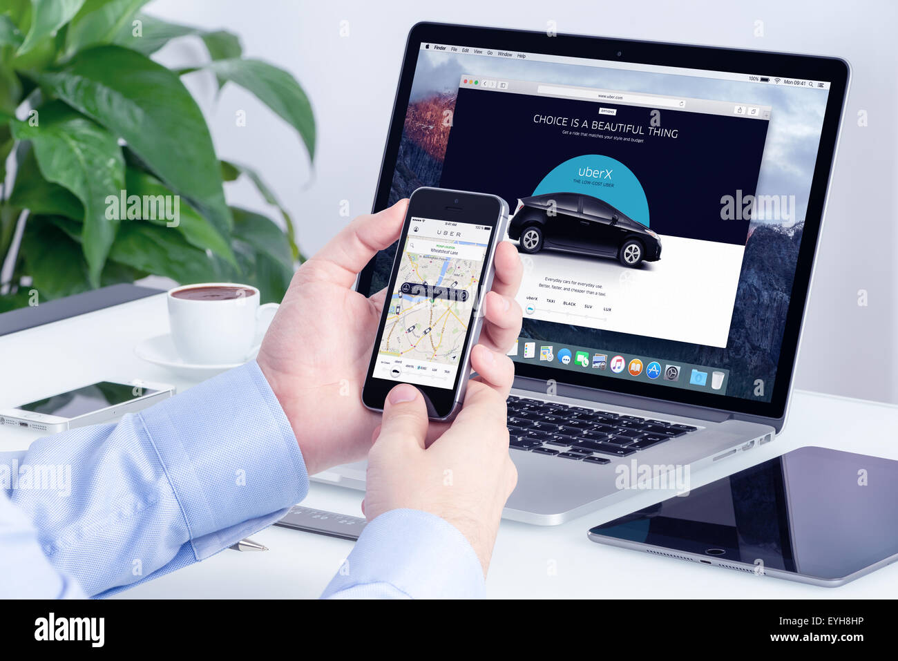 Varna, Bulgaria - 29 Maggio 2015: uomo ordini Uber X attraverso il suo iPhone e Macbook con sito web Uber sullo sfondo. Foto Stock