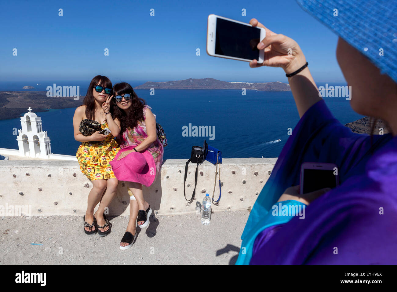 Giovani ragazze cinesi di scattare una foto sul telefono, punto di vista nel villaggio di Firostefani, sulla caldera. Santorini, isole greche, Grecia, Europa Foto Stock