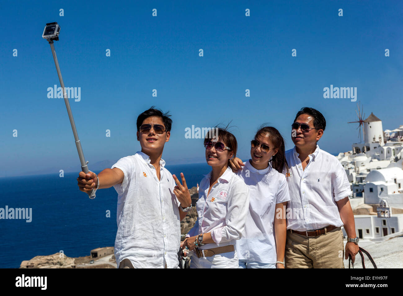 Turisti asiatici che scattano selfie su smartphone fotocamera Selfie Stick persone telefono di gruppo fare foto amici Isole greche Oia Santorini Grecia Europa Foto Stock