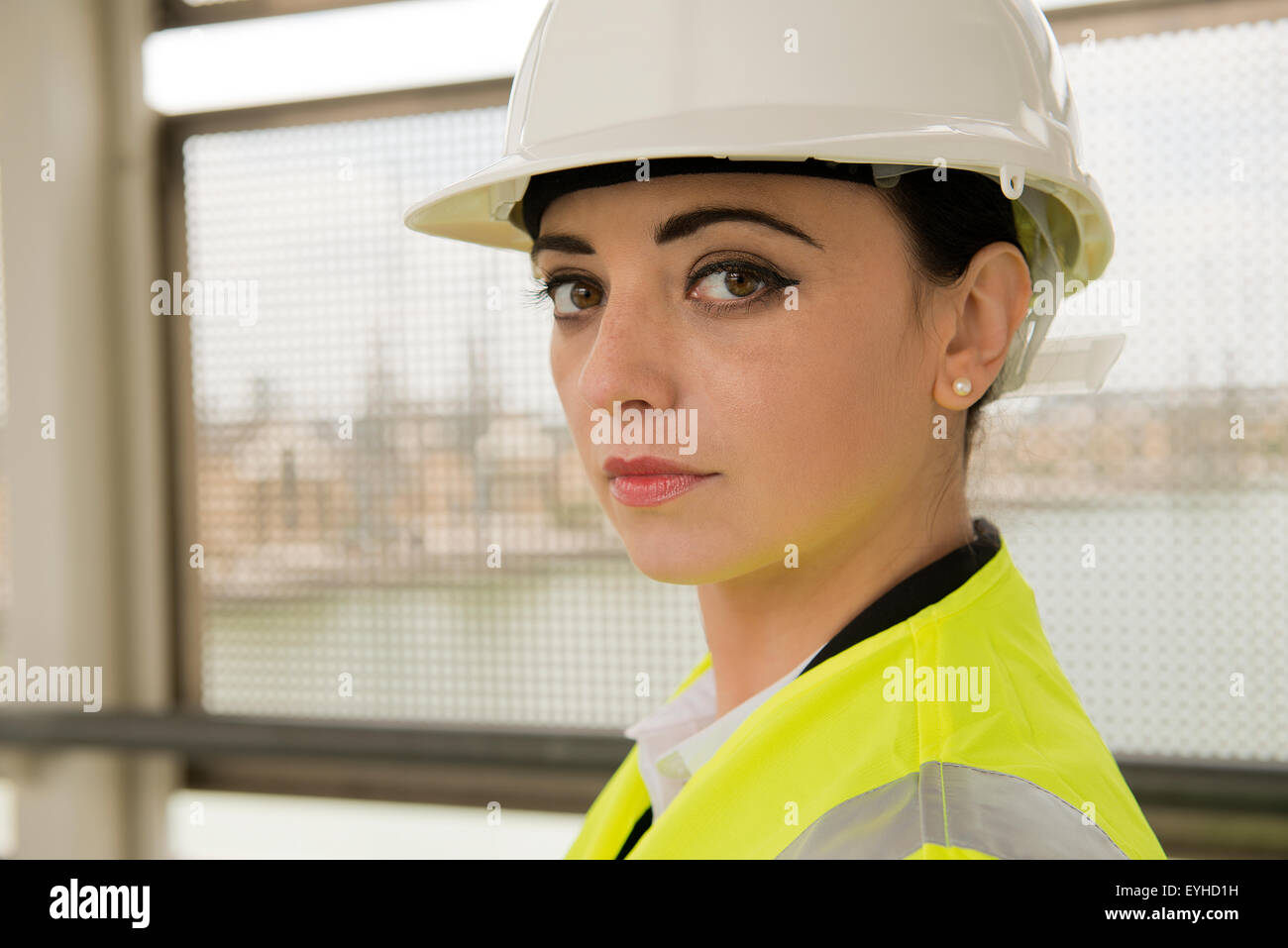 Giovane donna lavorando su un sito di costruzione, indossando un bianco di elmetto e un riflettente giubbotto di sicurezza. Foto Stock