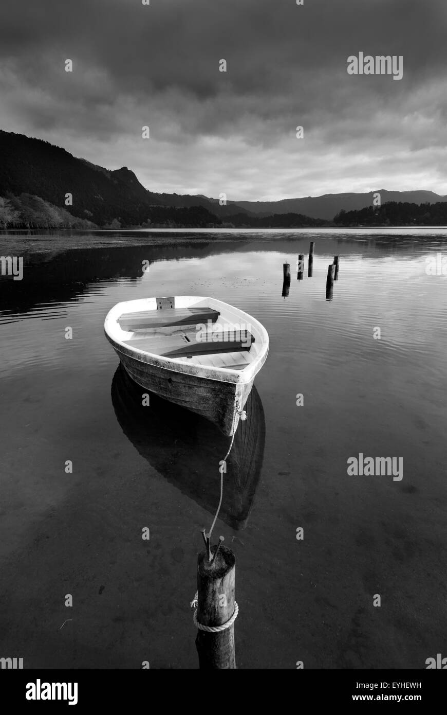 Piccola imbarcazione, legato ad un palo in un lago calmo con una tempesta di avvicinamento. Foto Stock