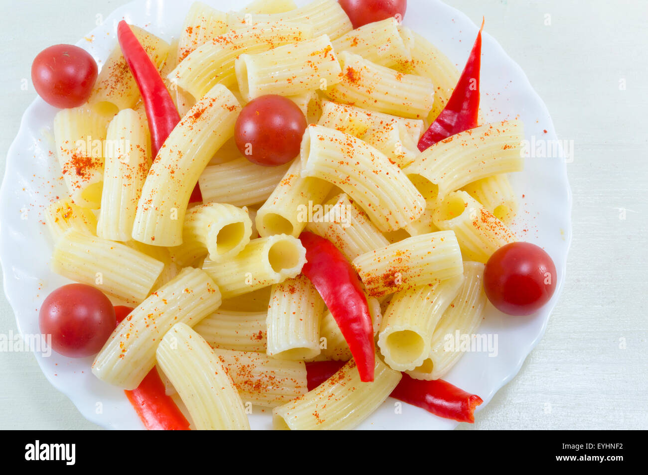 Pasta con pomodori ciliegia e pepe rosso servito in una piastra bianca su di un tavolo di legno vicino fino Foto Stock