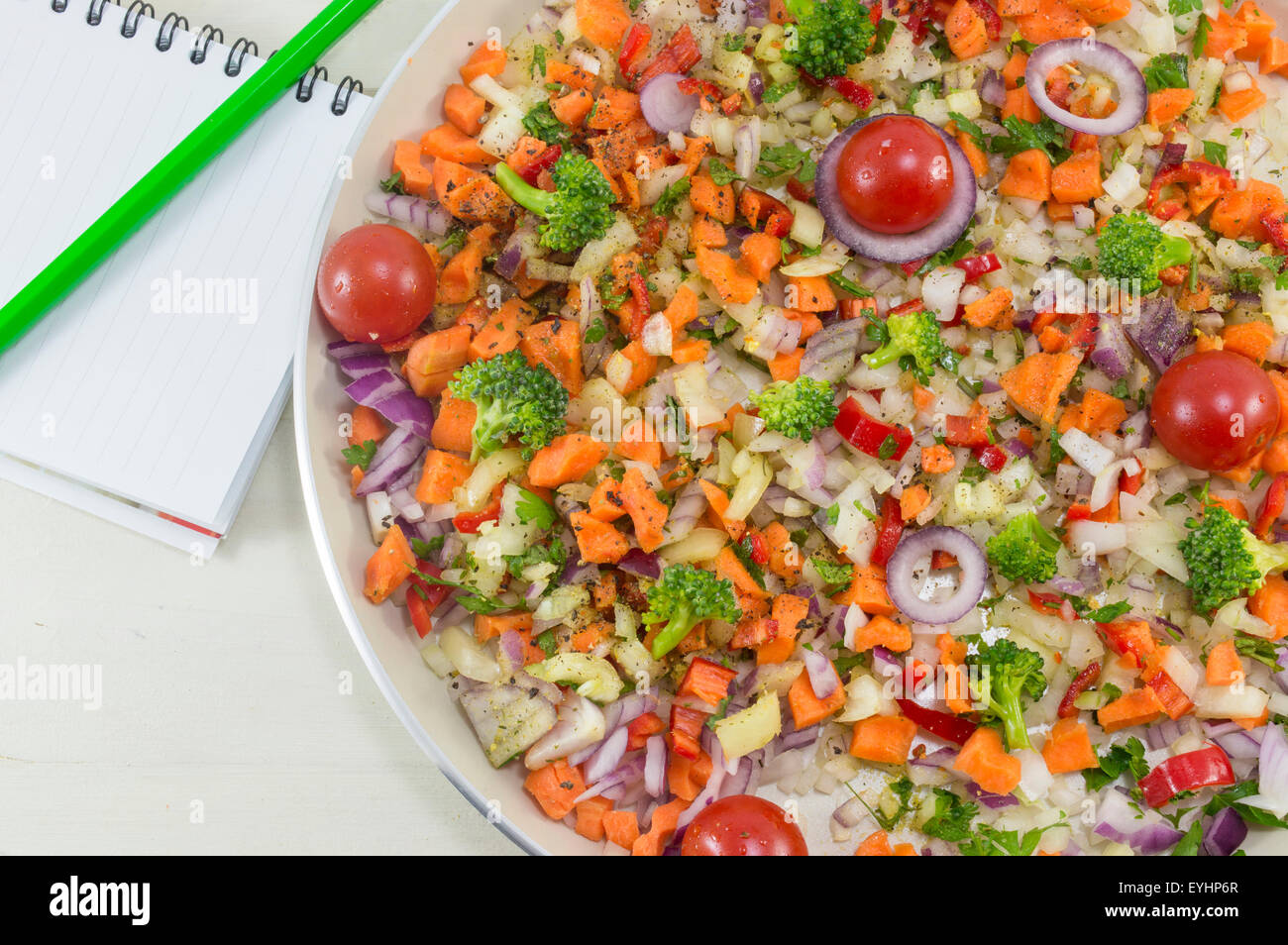Insalata di verdure su una piastra accanto a un quaderno e una penna per scrivere la ricetta. La cottura di cibo Foto Stock