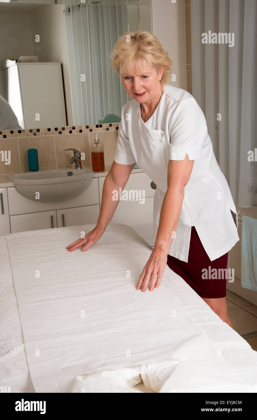 Massaggiatrice prepara il letto nella sua camera di trattamento Foto Stock