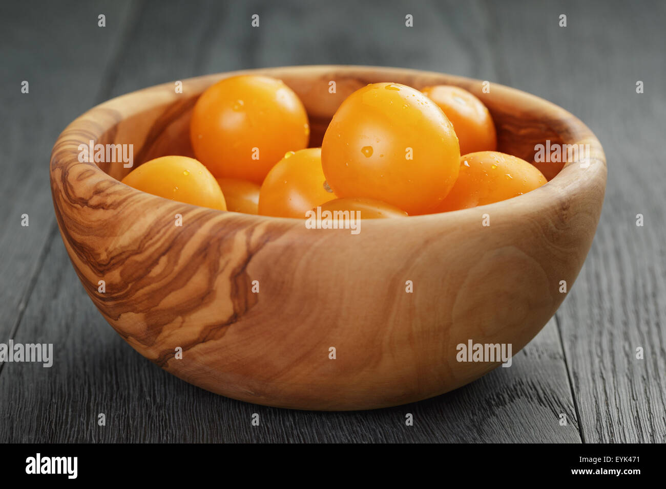 Giallo pomodori ciliegia nel recipiente di oliva sulla tavola di legno Foto Stock