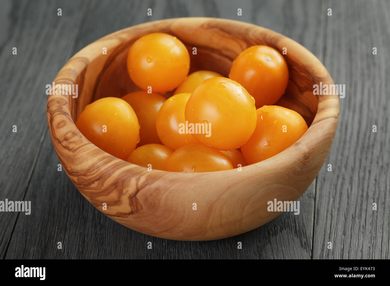 Giallo pomodori ciliegia nel recipiente di oliva sulla tavola di legno Foto Stock