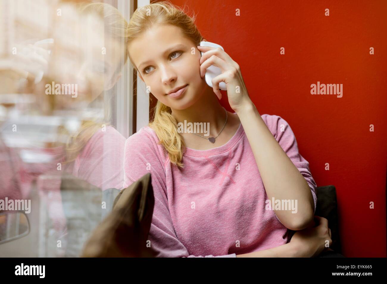 Giovane donna guardando fuori della finestra cafe mentre la chat sullo smartphone Foto Stock
