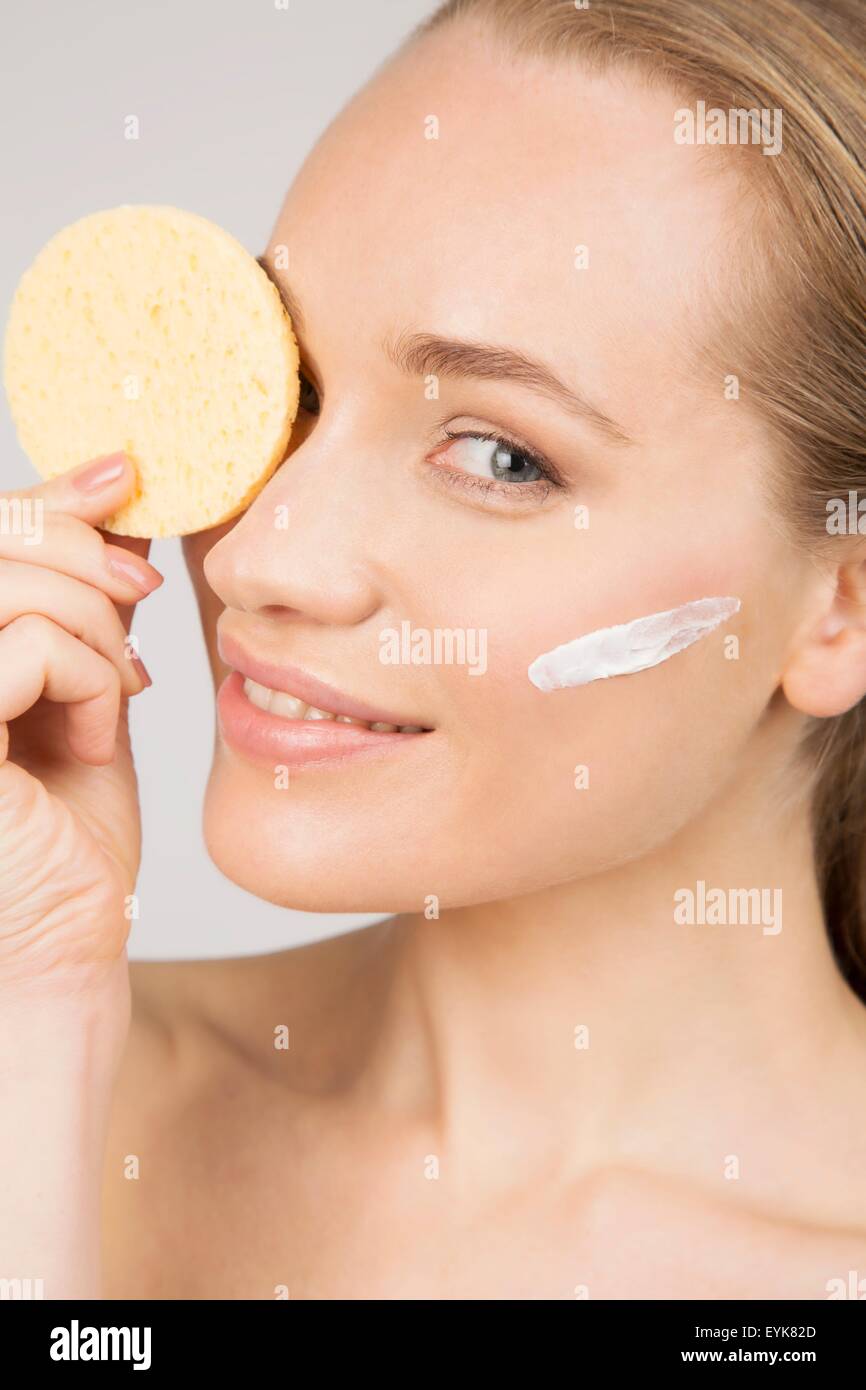 Ritratto di giovane donna con crema di bellezza sul viso, coprendo un occhio con il make-up spugna Foto Stock