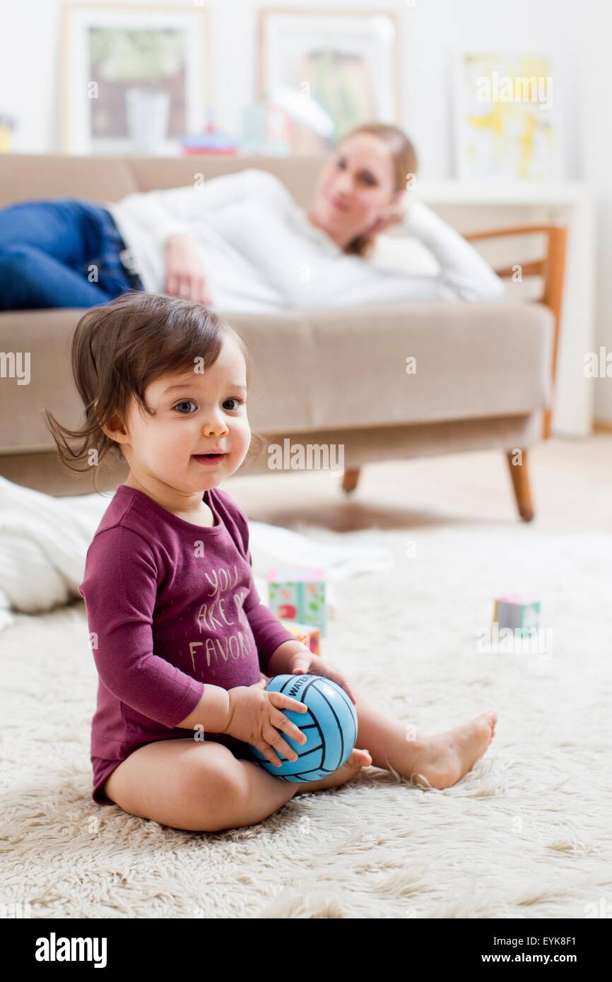 Madre sdraiato sul divano guardando baby boy giocare sul pavimento Foto Stock