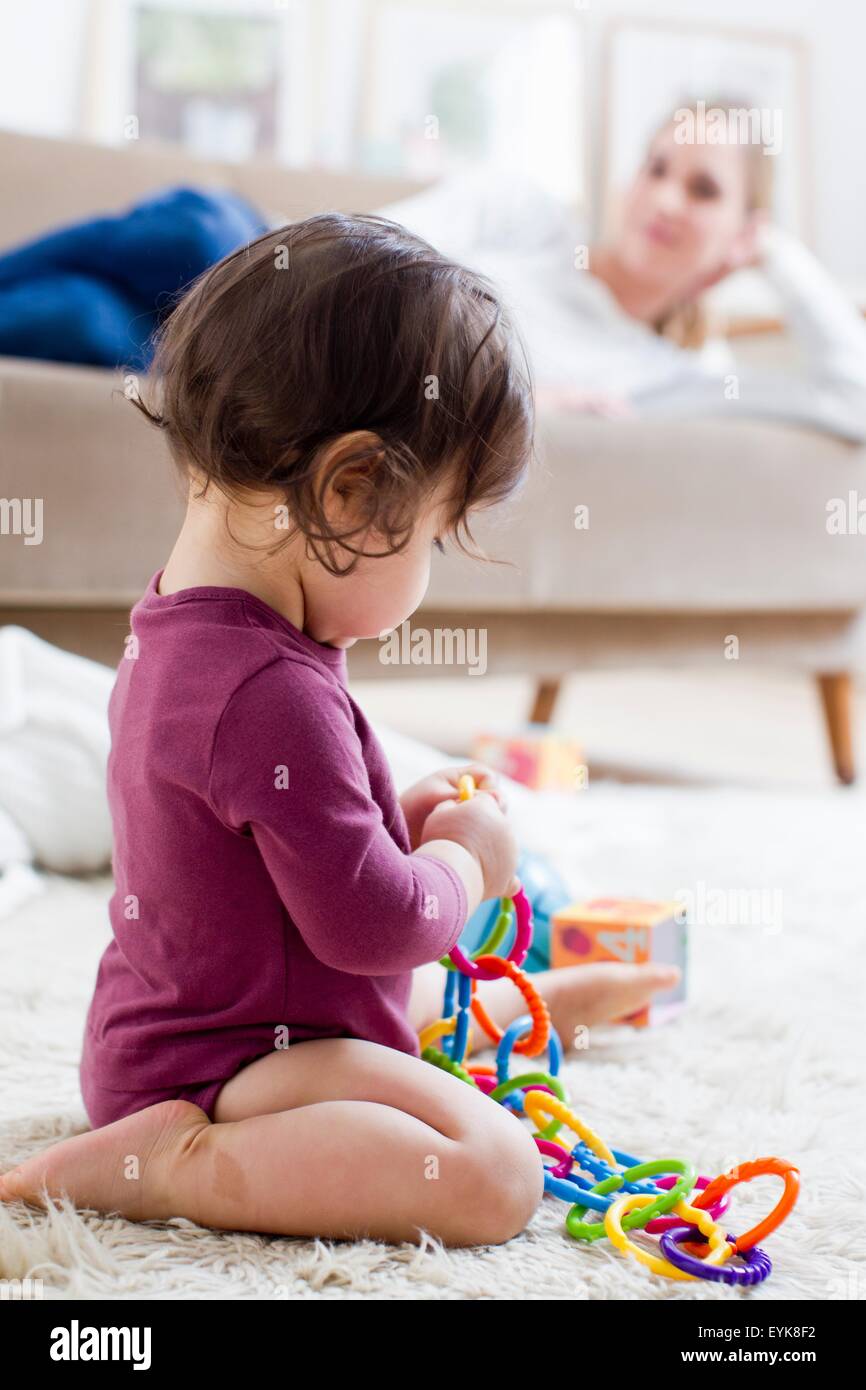 Madre sdraiato sul divano guardando baby boy giocare sul pavimento Foto Stock