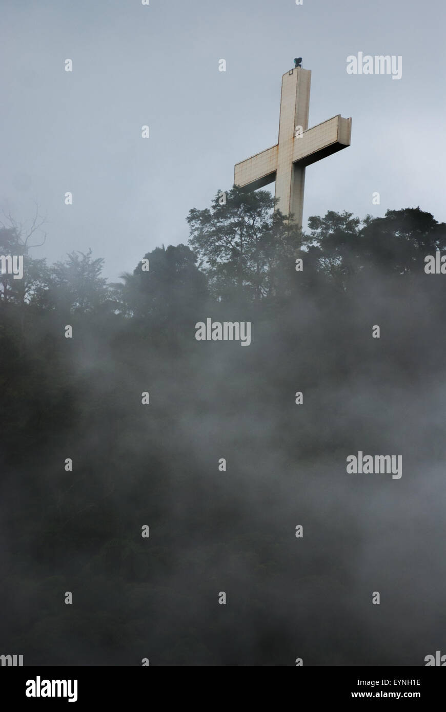 Un'alta croce cristiana emerge attraverso la nebbia su una cresta che conduce alla vetta piatta del Bukit Kasih a Kanonang, Minahasa, Sulawesi settentrionale, Indonesia. Foto Stock