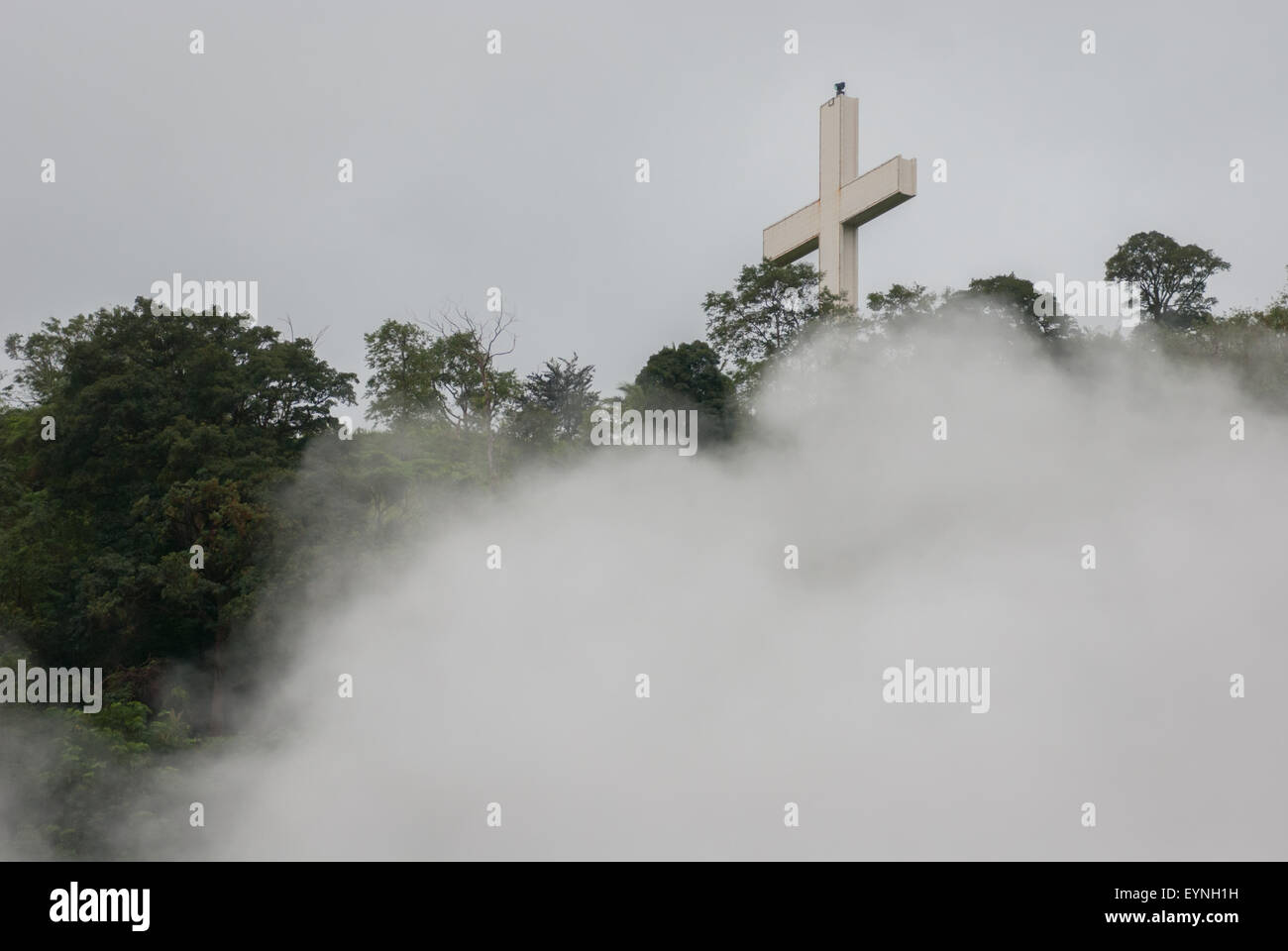 Un'alta croce cristiana è vista attraverso la nebbia su un crinale a Bukit Kasih, una popolare destinazione turistica religiosa a Minahasa, Sulawesi Nord, Indonesia. Foto Stock