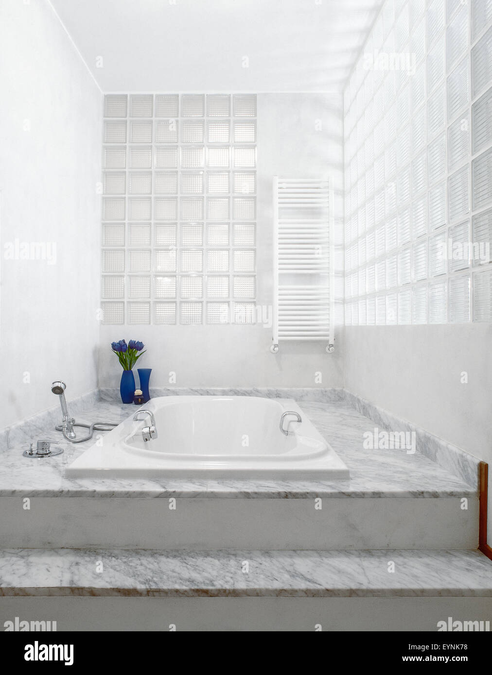 Primo piano di una vasca incassata nell'accesso rialzato piano di marmo nella stanza da bagno molto moderna con un muro fatto di mattoni in vetro Foto Stock