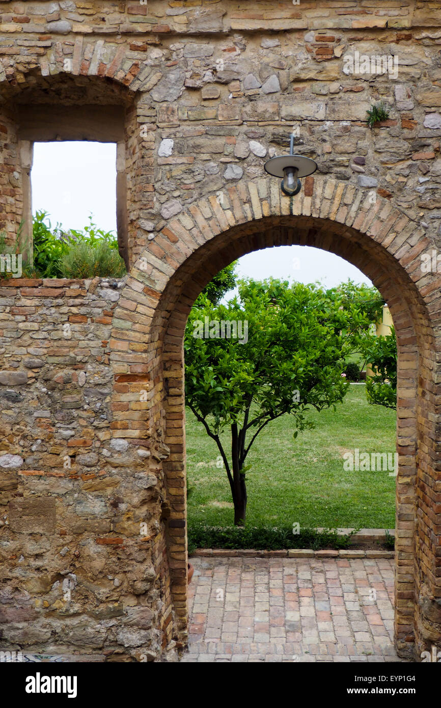 Arcata in pietra e un muro di mattoni che conduce a un giardino. Foto Stock