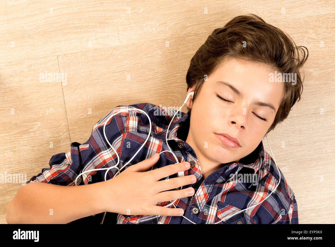 Ritratto di un ragazzo in ascolto di musica con le cuffie tesa su di un pavimento in parquet a casa Foto Stock