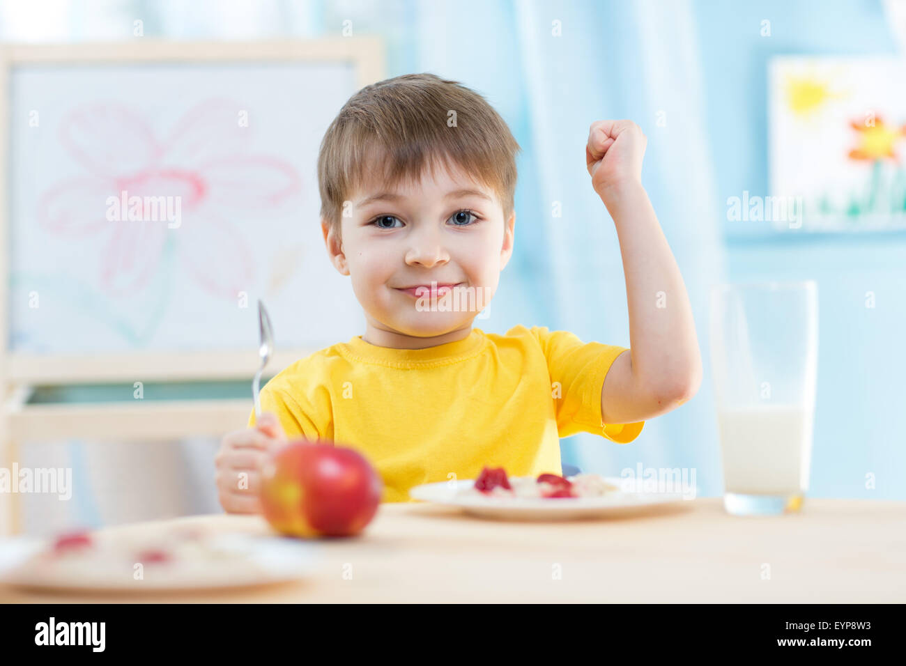 Bambino mangia il cibo sano che mostra la sua forza in ambienti interni Foto Stock