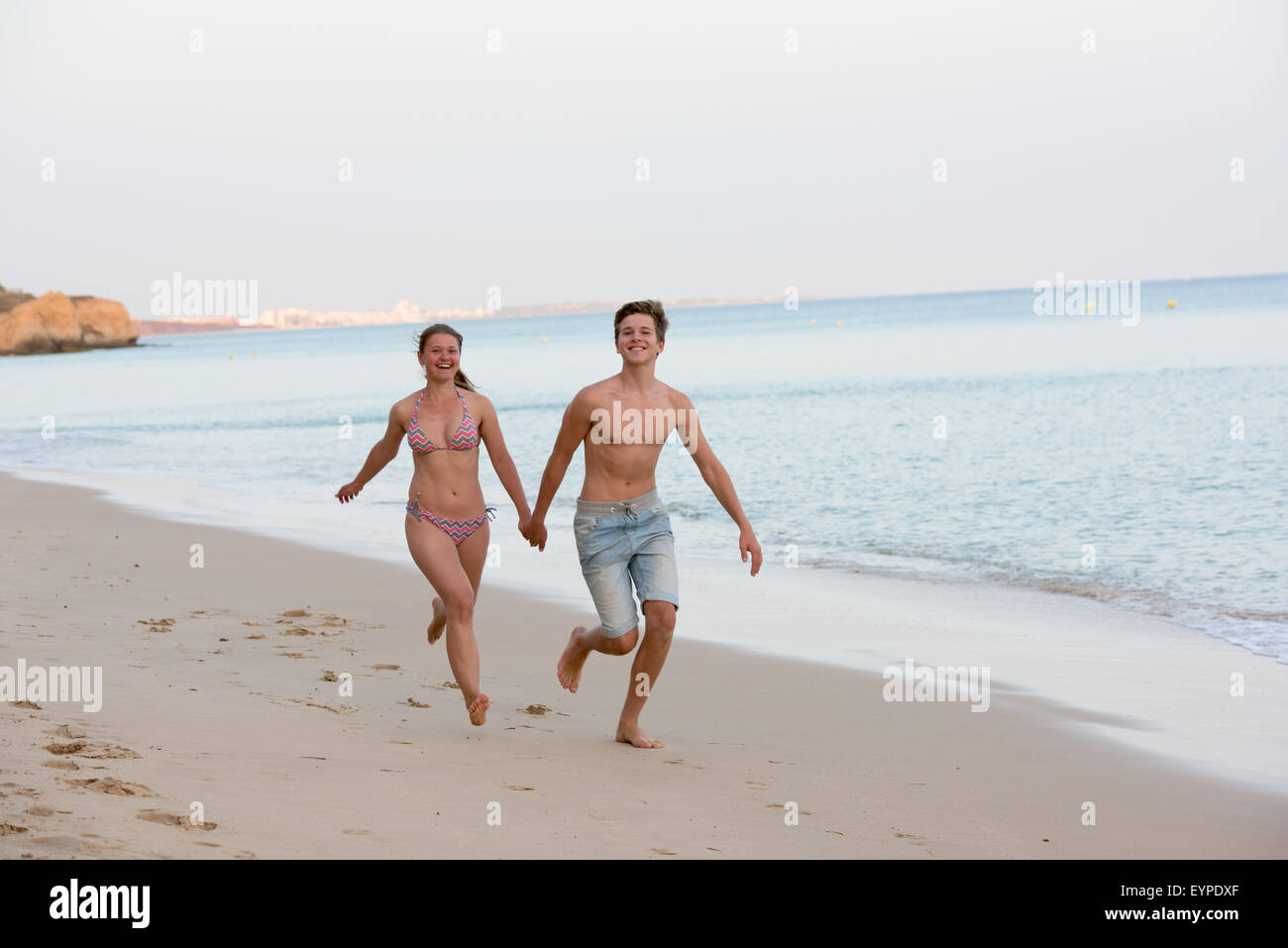 Felice coppia giovane in esecuzione e tenendo le mani su una spiaggia Foto Stock