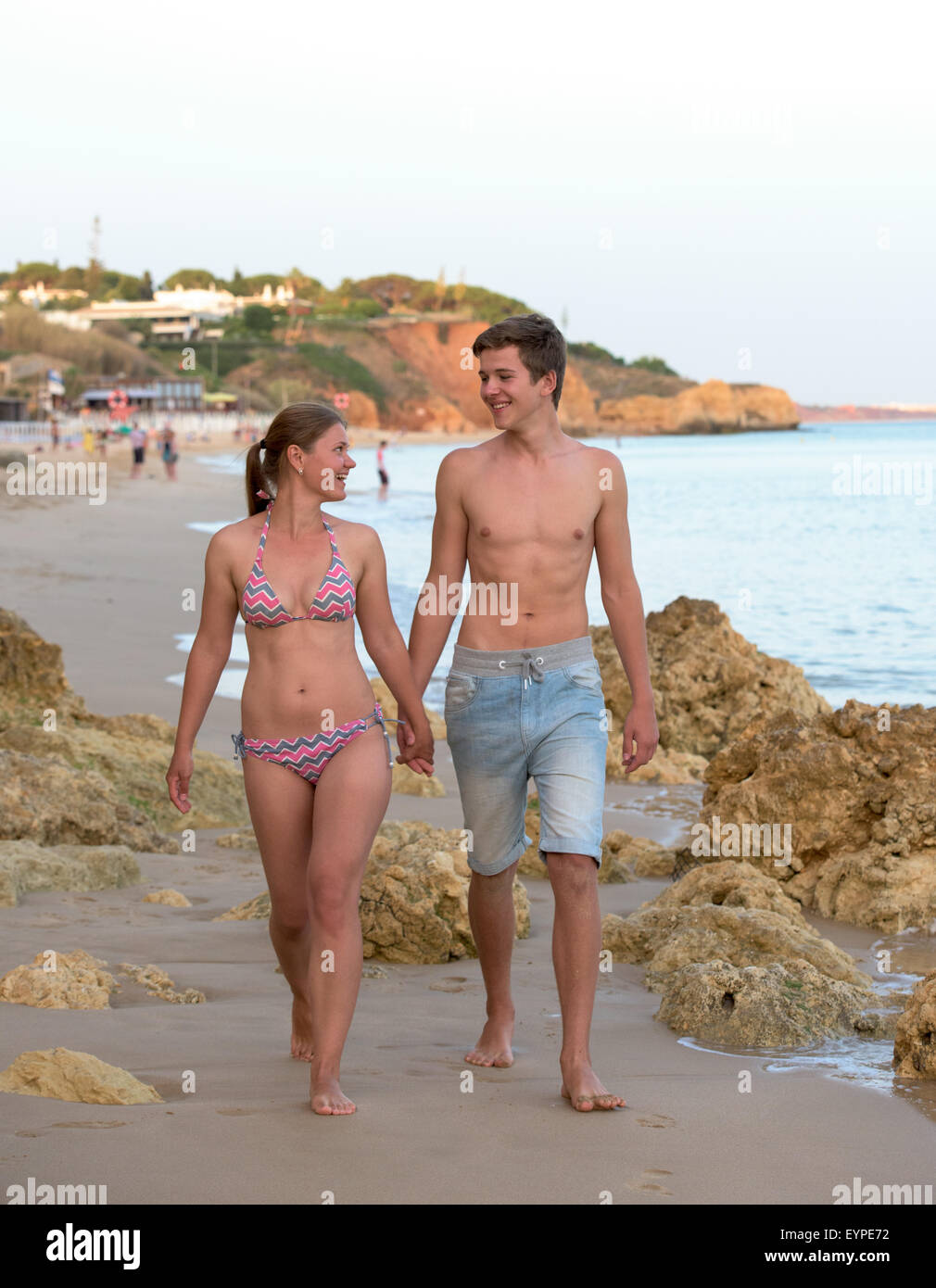 Felice coppia giovane di camminare sulla spiaggia tra rocce e tenendo le mani su una spiaggia Foto Stock