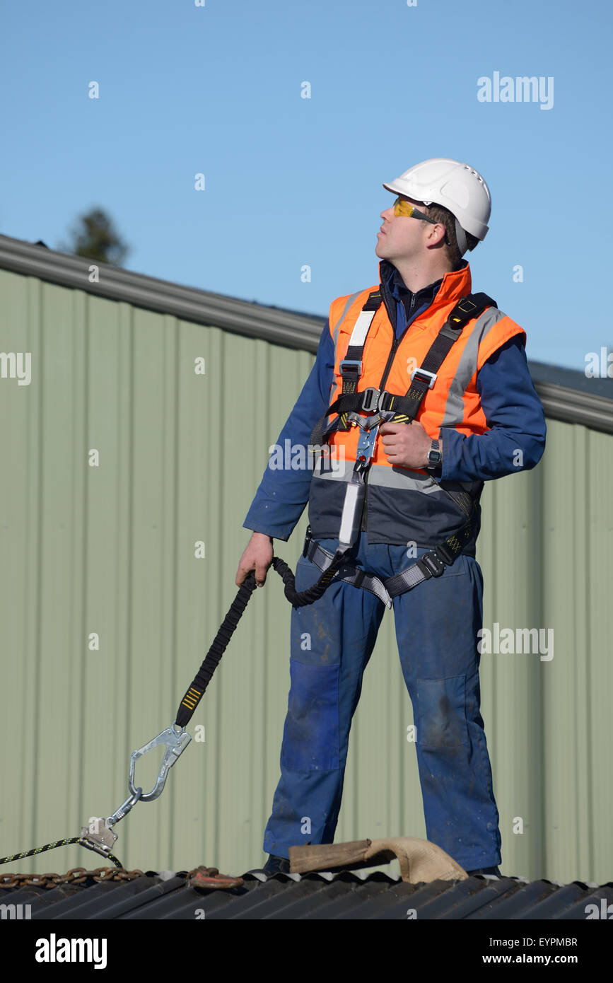 Un costruttore che indossa una imbracatura di sicurezza mentre si lavora ad altezze attende istruzioni dal caposquadra Foto Stock