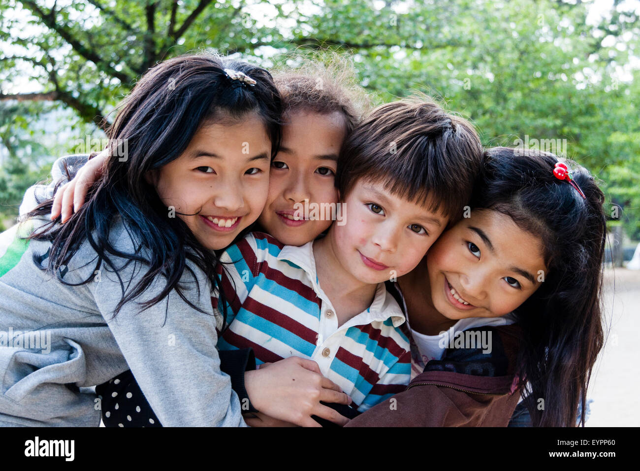Fila di quattro bambini sorridenti, 7-9 anni, testa e spalle, le facce rivolte viewer con contatto visivo. 3 ragazze giapponesi e un ragazzo caucasico. Avvolgente. Foto Stock