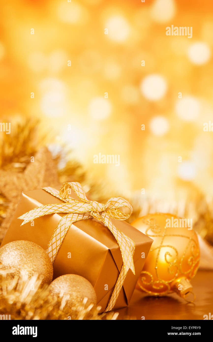 Golden baubles di Natale e un dono di fronte sfocati luci d'oro. Foto Stock