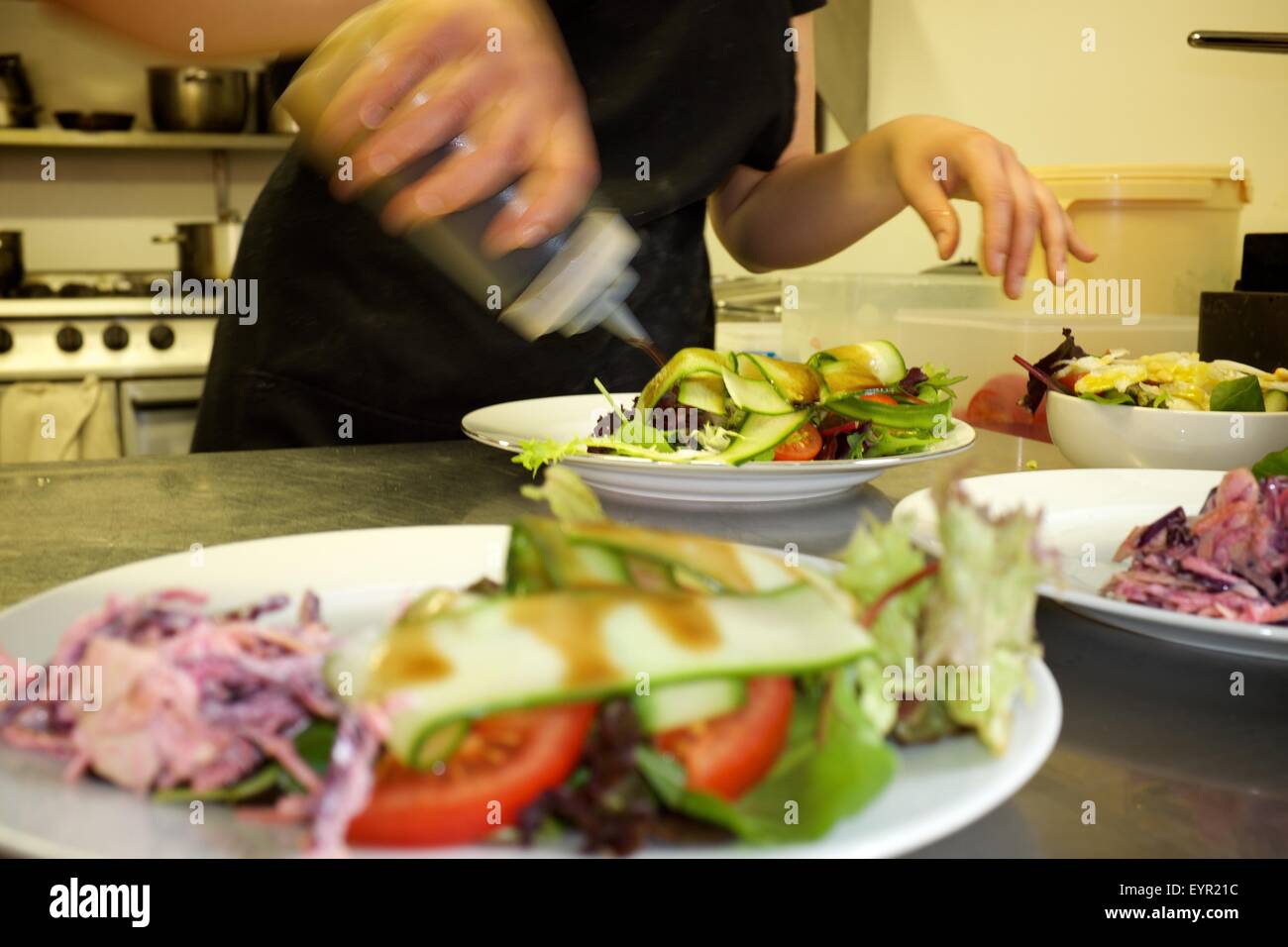 Una femmina di chef le piastre su abiti e insalata in un professionista cafe cucina Foto Stock