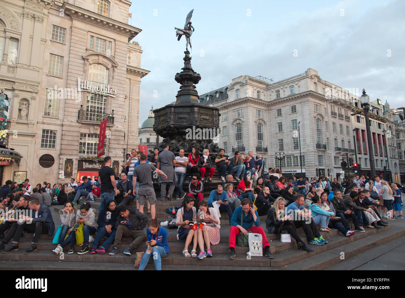 Turisti che si siedono sui gradini della struttura Shaftesbury Memorial Fontana e la statua di Eros, Piccadilly Circus, London, England, Regno Unito Foto Stock