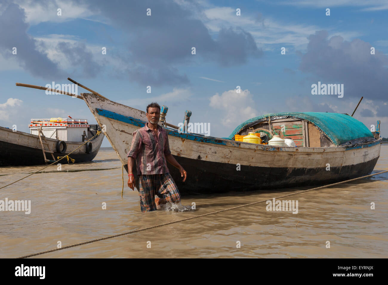 Ritratto di un uomo e di una barca di legno su un porto di fiume della comunità a Haldia, Bengala occidentale, India. Foto Stock