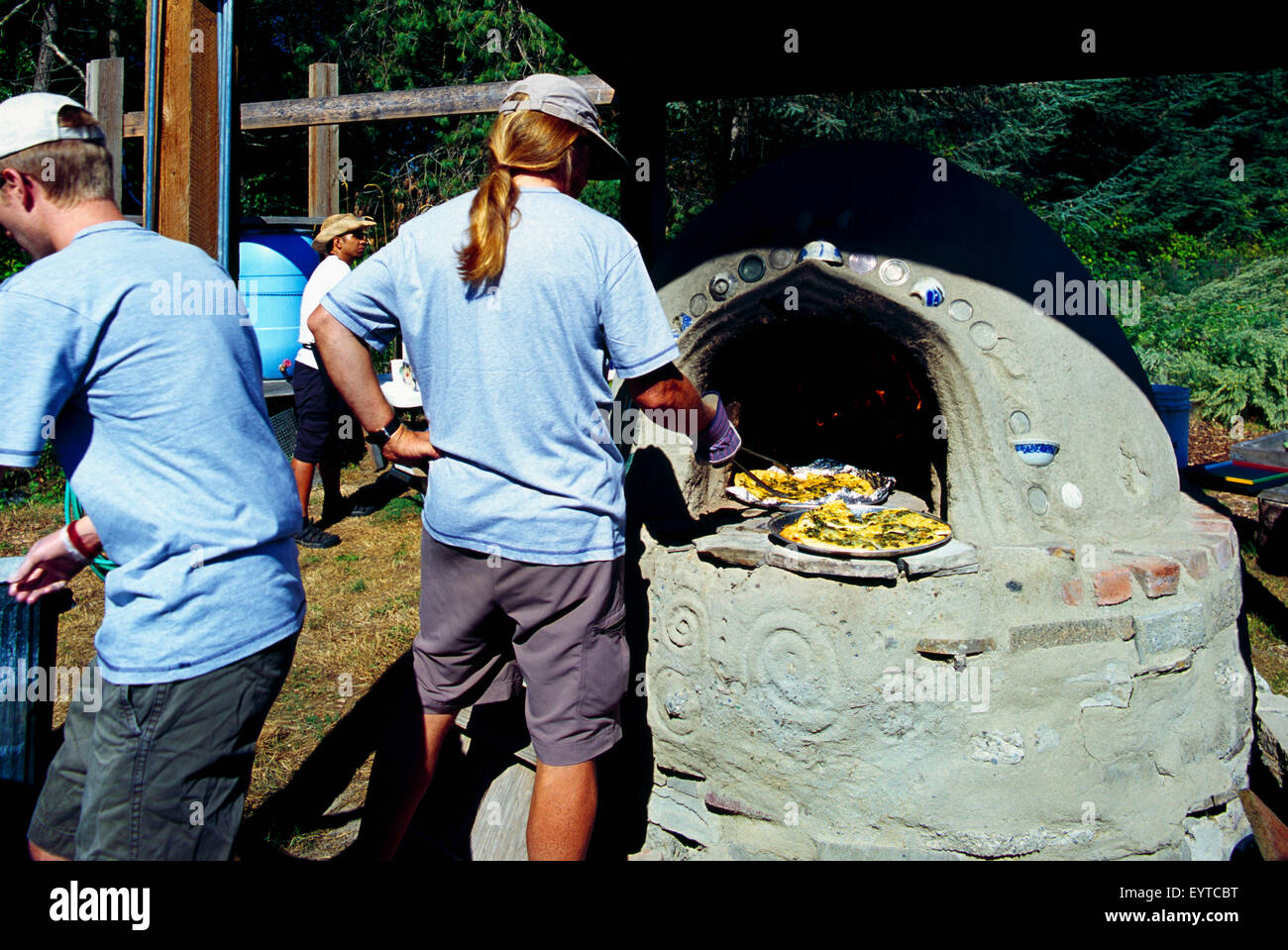 Uomo di lavoro con una lunga coda di cavallo la cottura aglio pane in Outdoor Legna per la stufa di Cob al Festival di aglio Foto Stock