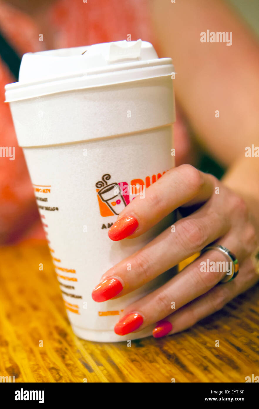 Donna con mano dipinto luminosamente unghie tenendo una tazza di Dunkin' Donuts caffè Foto Stock