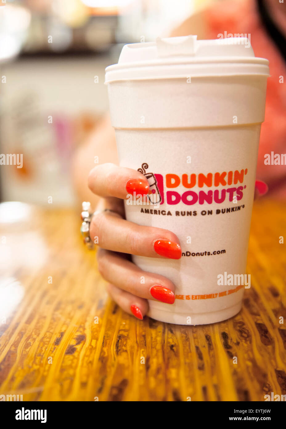 Donna con mano dipinto luminosamente unghie tenendo una tazza di Dunkin' Donuts caffè Foto Stock