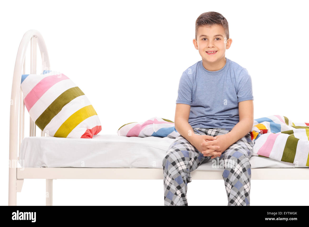 Ragazzo pigiami blu seduta su di un letto e guardando la telecamera isolato su bianco Foto Stock