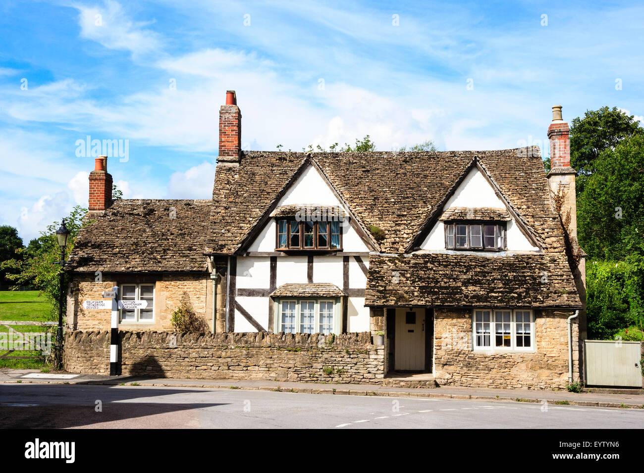 Inghilterra, Lacock, Cotswolds. Grande medievale graticcio e gesso house con tradizionale in bianco e nero British segno posto all'esterno. Foto Stock