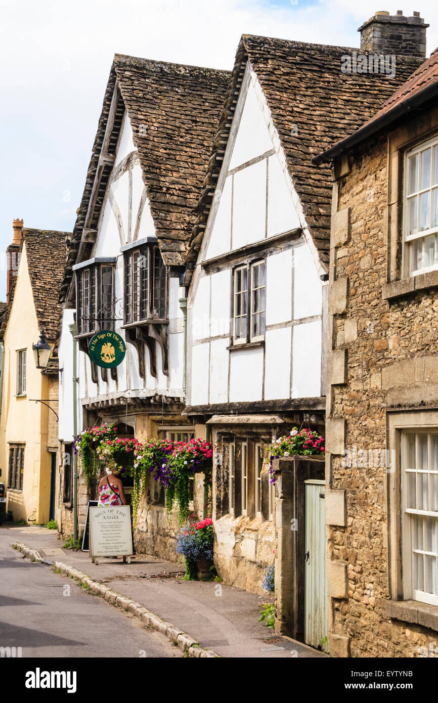 Inghilterra, Lacock. Vista lungo la cinquecentesca chiesa pittoresca street, i due piani di segno del Angel Inn, un legname e l'intonaco bianco taverna. Foto Stock