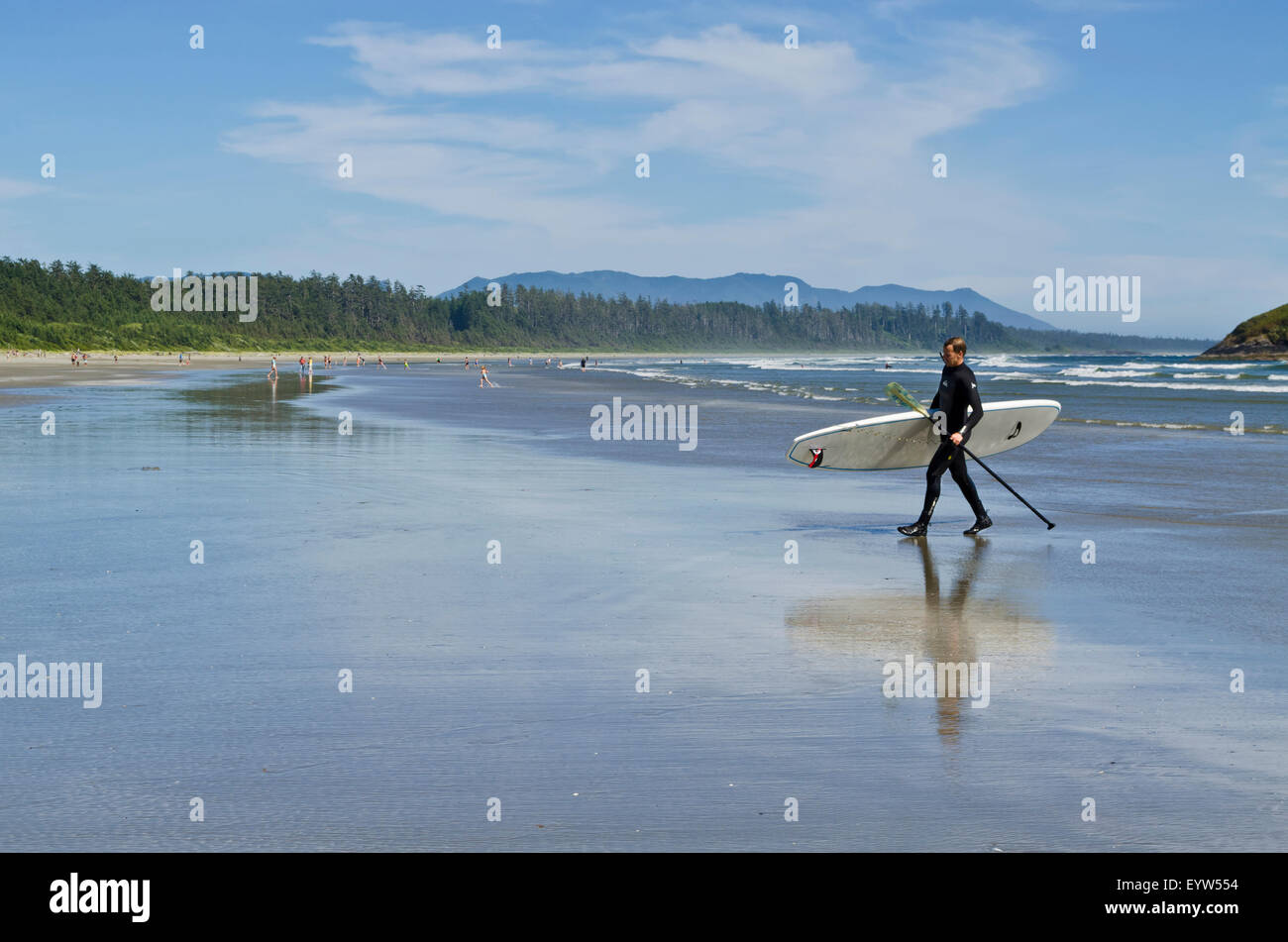 L uomo nella muta di camminare sulla spiaggia con il suo stand up paddleboard dopo paddleboarding a lunga spiaggia vicino a Tofino, BC. Foto Stock