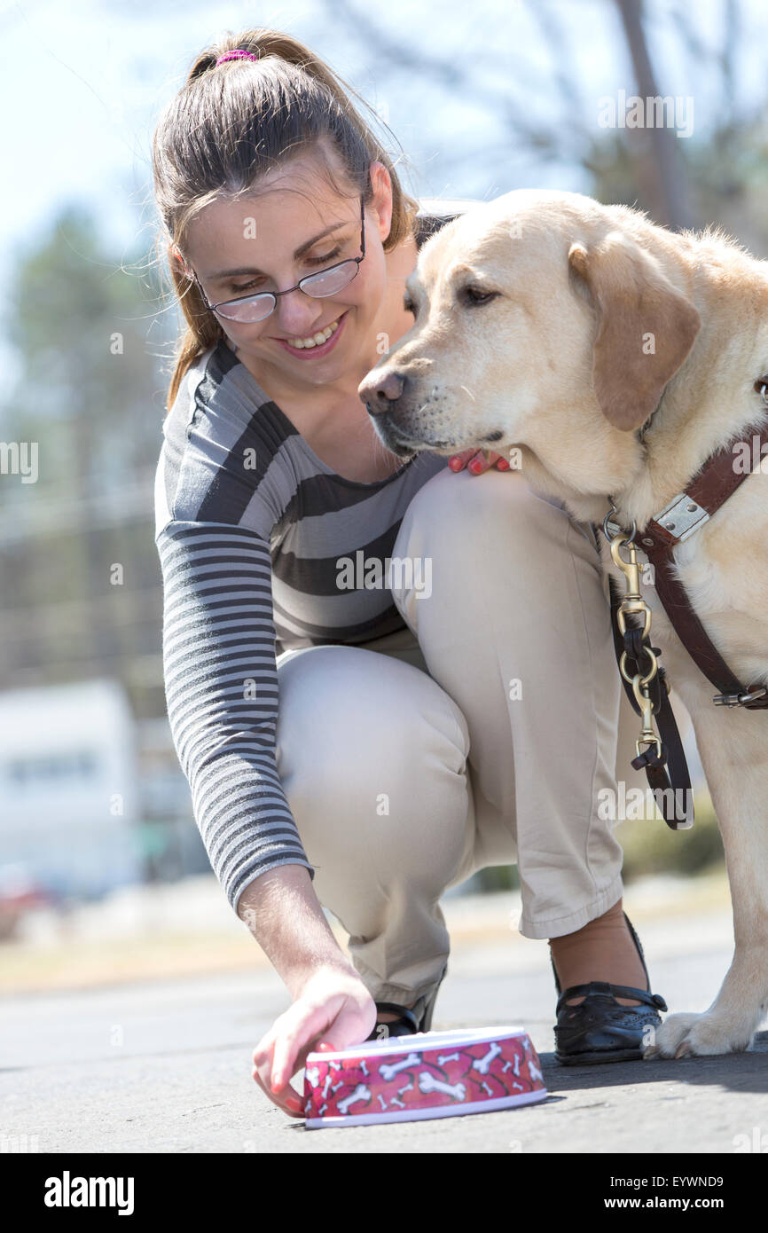 Giovane donna con una minorazione visiva alimentando il suo cane di servizio Foto Stock