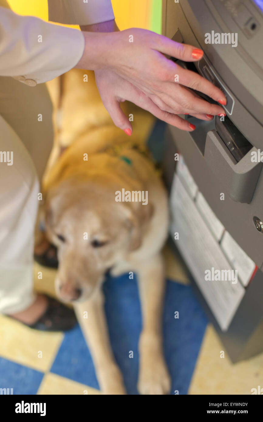 Giovane donna cieca utilizzando una banca ATM con il suo cane di servizio in attesa Foto Stock